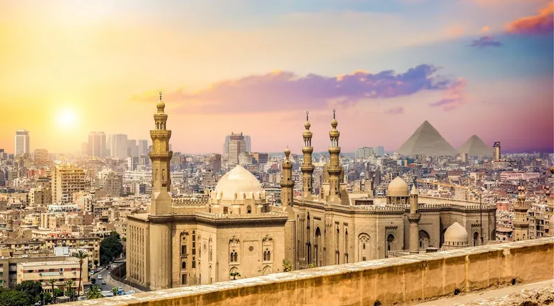 Cairo skyline at sunset with the Sultan Hassan Mosque and the Pyramids of Giza in the distance