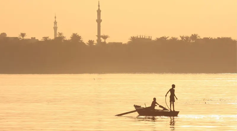 Silhouette of a small boat on the Nile River at sunset with mosque minarets on the skyline