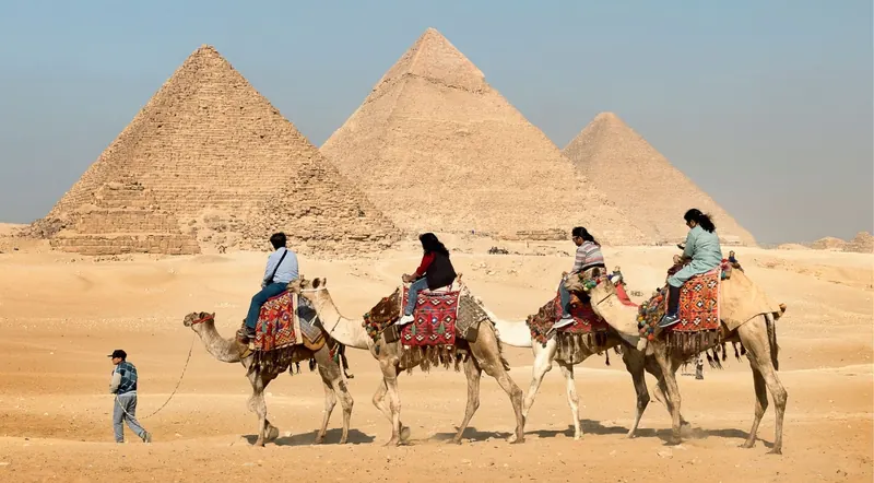 Camel riders passing in front of the Great Pyramid and the other pyramids of Giza